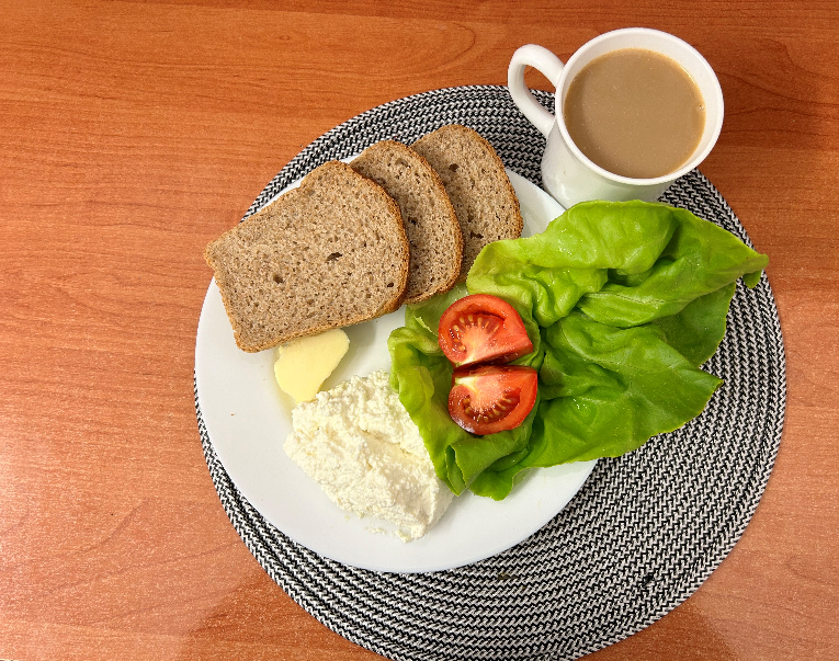 Na zdjęciu: Kawa z mlekiem, Chleb Graham, Masło extra 82%, Twarożek, Pomidor, Sałata zielona